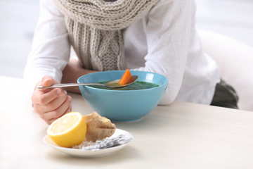 Sick little boy eating broth to cure cold at table in kitchen