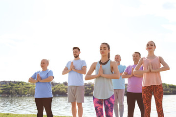 Obraz premium Group of people practicing yoga near river on sunny day