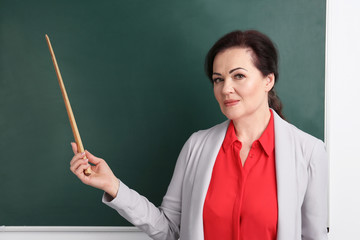 Portrait of female teacher with pointer near chalkboard in classroom