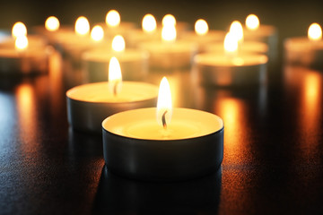 Wax candles burning on table in darkness, closeup