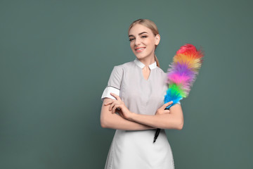 Young chambermaid with dusting brush on color background