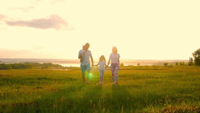 Happy Young Family with two children running on summer field. Healthy mother, father and little children enjoying nature together, outdoors at sunset.