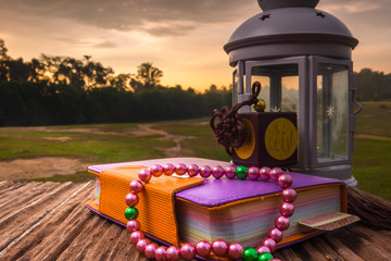 Quran, beads, and lantern on old wood with a beautiful sunrise as background. Ramadhan Concept.