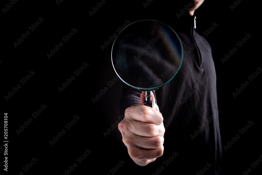 Wall mural man's hand, holding classic styled magnifying glass on a black background