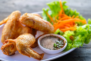 Fried chicken in a white dish with vegetables and dipping sauce on a wooden table.