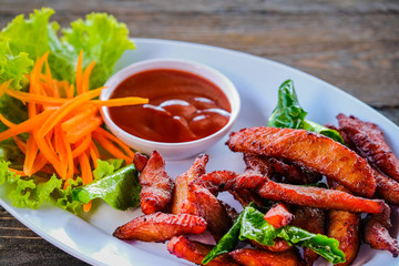 Pork fried in a white dish with vegetables and dipping sauce on a wooden table.