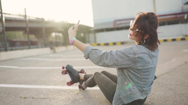 Outdoor portrait of young attractive female in stylish outfit making a selfie. Shooting on the phone camera