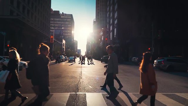 People crossing busy downtown street with background traffic during golden hour
