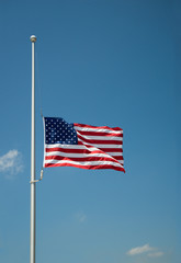 Obraz premium The United States flag flying at half-mast or half-staff on a flagpole. Blue sky background with copy space.