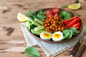 Buddha bowl, healthy and balanced food. Fried chickpeas, cherry tomatoes, cucumbers, paprika, eggs, spinach, arugula