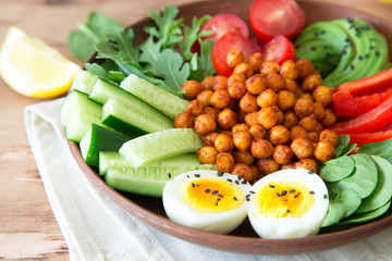 Buddha bowl, healthy and balanced food. Fried chickpeas, cherry tomatoes, cucumbers, paprika, eggs, spinach, arugula