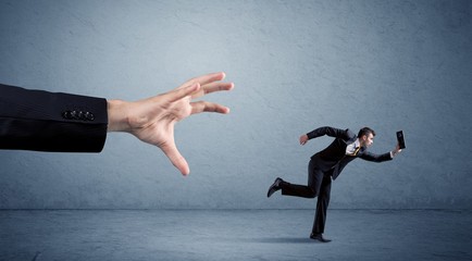 Young miniature businessman running from a big hand with blue background