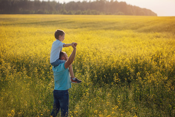 Father holding his son on the shouldders and standing on nature summer background.