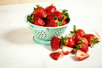 fresh red strawberries in a small colander on a white wooden table