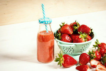 fresh red strawberries in a small colander and drink on a white wooden table