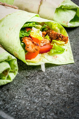 Mexican food. Healthy eating. Wrap sandwich: green lavash tortillas with spinach, fried chicken, fresh greens salad, tomatoes, yoghurt sauce. Black dark stone table. Copy space
