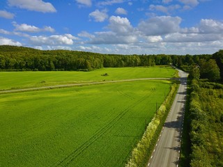 Cultivated field aerial view with road and large forest in the background and blue sky above, Summer in Sweden