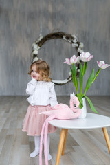 Fashionable little girl posing at a table on which there is a vase with a tulip