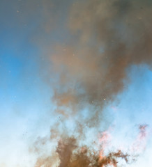 Photo of thick heavy brown yellow smoke from burning branches of pine tree, birch, spruce and other trees from swedish forest with flying ash and other fire products pieces in big bonfire, blue sky