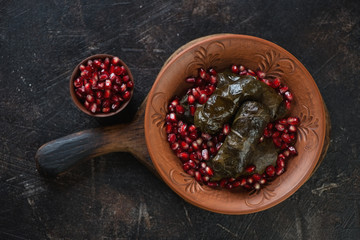 Clay plate with dolma or dolmades and pomegranate seeds on a dark brown stone background, top view, horizontal shot