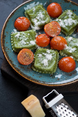 Spinach ravioli served with cherry tomatoes and parmesan cheese on a turquoise plate, close-up