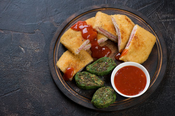 Rustic wooden serving board with sliced chicken cordon bleu stuffed with cheese and ham, studio shot
