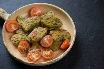 Serving pan with vegetable nuggets and cherry tomatoes over black stone background, horizontal shot with space