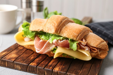 Tasty croissant sandwich with bacon on table