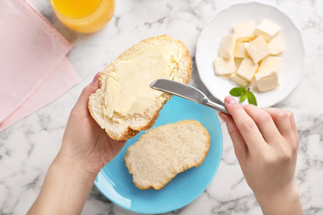 Woman spreading butter on slice of bread over table, closeup