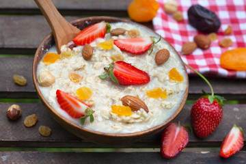 Oatmeal Porridge with Strawberries and dried fruit on wooden table. Healthy Breakfast made from oat flakes, nuts and fruit.