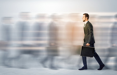 Young businessman with briefcase hurry up on a crowded street with blurred people around
