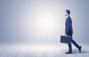Successful businessman walking in front of an empty wall with briefcase on his hand
