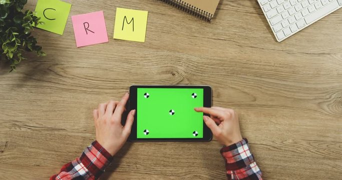 Close up on the woman's hands taping on the black horizontal tablet device with a green screen on the wooden table. SRM. Chroma key. Tracking motion