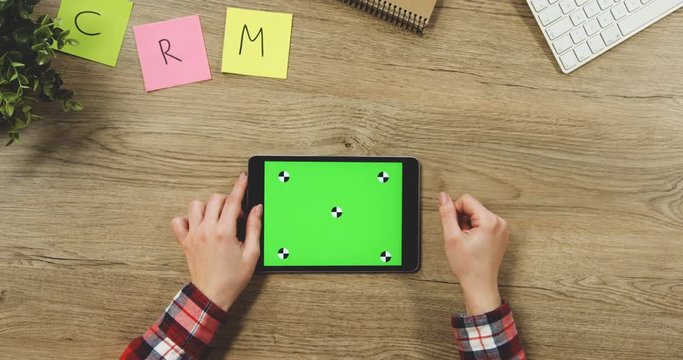 Close up on the woman's hands taping on the black horizontal tablet device with a green screen on the wooden table. SRM. Chroma key. Tracking motion