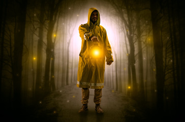 Man in raincoat coming from dark forest with glowing lantern in his hand concept
