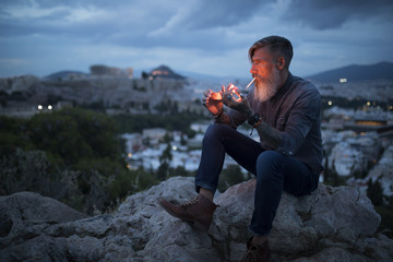 Portrait eines bärtigen Mannes, der auf dem Berg von Athen raucht und die blaue Stunde genießt