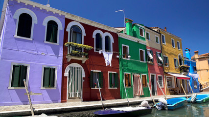 Fototapeta na wymiar Brightly colored houses and boats at mooring points along canal on Burano island