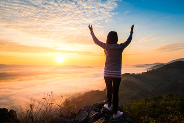 Fototapeta na wymiar Young woman standing on top of the mountain watching the sun rise with fog