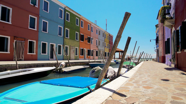 Burano island canal with motorboats moored along street with colorful buildings
