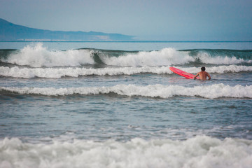 Man with a red surf swimming to a wave. Famara beach, Lanzarote, Canary Islands, Spain.