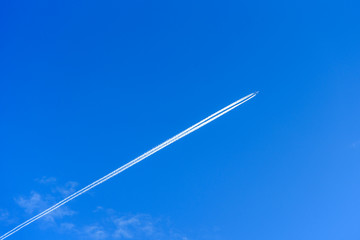 A distant aircraft with long diagonal condensation trails or contrails on a blue sky day