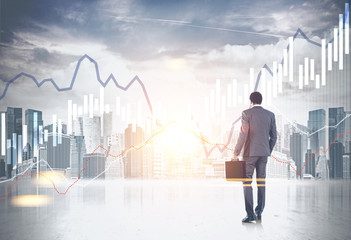 Businessman with suitcase looking at graphs in sky