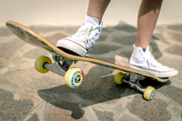 Teenager enjoying free time training on the skateboard. Closeup of the legs and the skate. Practice freestyle making a trick. Concept image of a skater rising a multicolor board on two wheels.