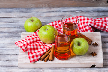 Apple juice in glasses, spices and apples on wooden cutting table 