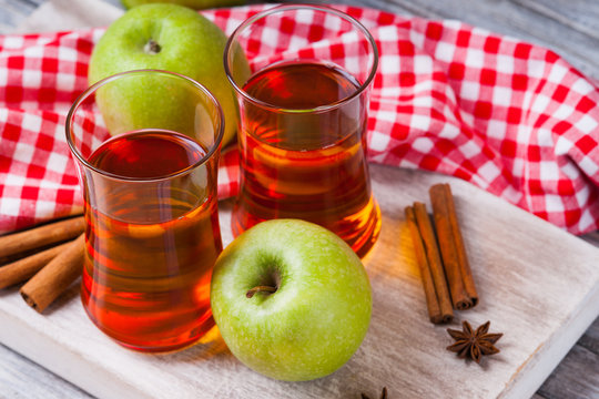 Apple juice in glasses, spices and apples on wooden cutting table