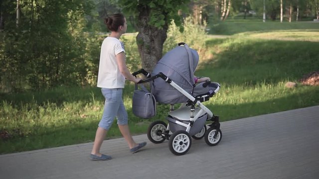 Mother walking with baby in baby carriage, carries a stroller, sideshot