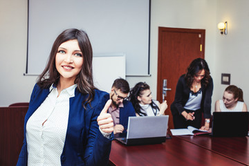 Happy successful businesswoman in the office with colleagues in the background.