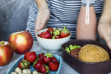 A woman's mother prepares her child for lunch in school and puts a sandwich and strawberries with peanuts in a lunchbox. Feeding children in the school concept