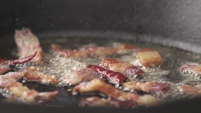 Bacon and chili sizzling in white wine in slow motion, camera pans left to right