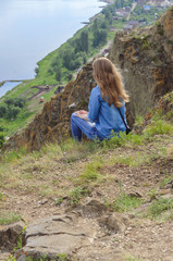 Naklejka na ściany i meble A girl in blue clothes is sitting on the edge of a cliff